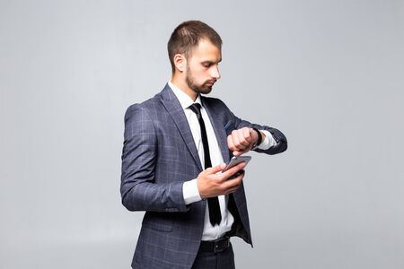 On the way to success. Young attractive businessman, talking on a smartphone, smiles and looks at his watch on a white backgroundの写真素材