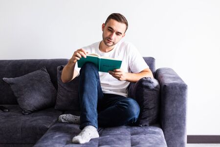 Smiling relaxed man reading a book lying on sofa