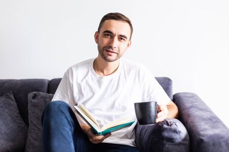 Young man having coffee while reading book in living room