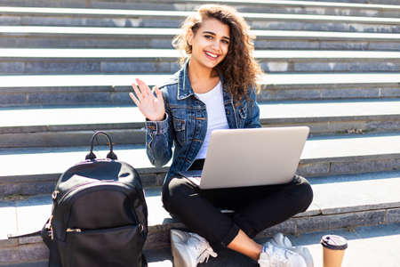 A young woman with a laptop sitting on the stairs, near the universityの写真素材