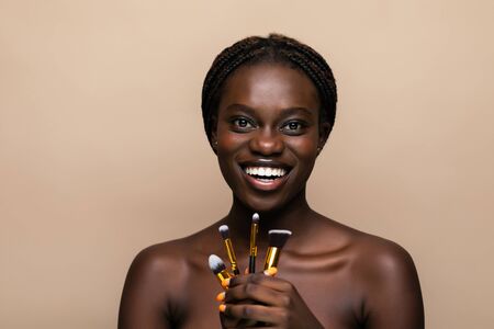 Beautiful african woman with makeup brushes near her faceの写真素材