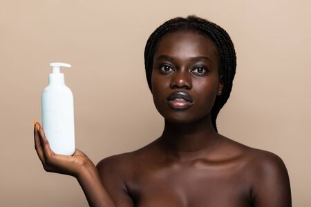 Beautiful woman applying face lotion on cheek. Beautiful intimate girl with perfect and healthy skin feeling shy isolated on beige background.の写真素材