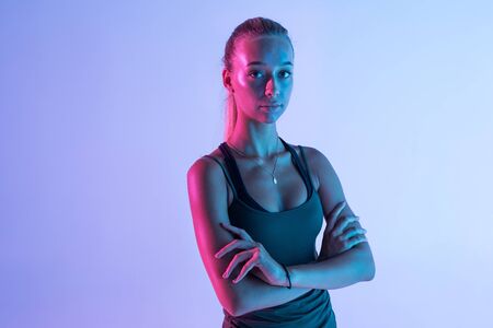 Full body of young smiling woman in sports wear, over violet light background