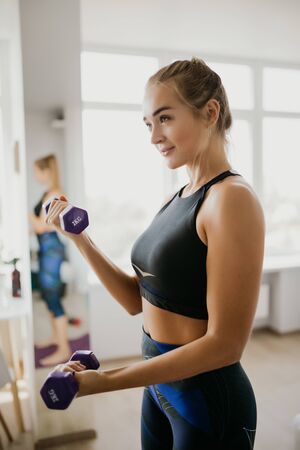 Sporty woman exercising with dumbbell at home to stay fitの写真素材