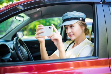 Smiling woman taking selfie picture with smart phone camera outdoors in car