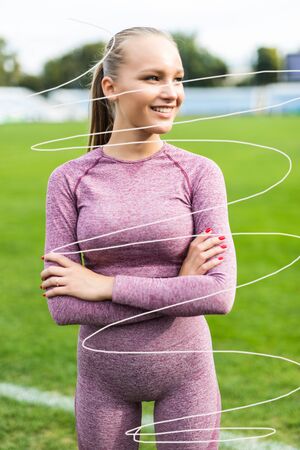 Portrait of fit young woman in sportswear standing on racetrack with her hands folded and looking...
