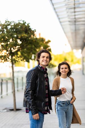 Happy to be together. Rear view of beautiful young couple holding hands and looking at each other with smile while walking through the city streetの写真素材
