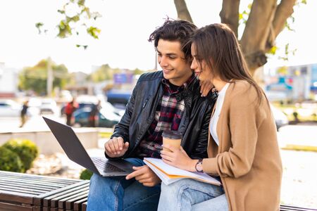 Happy young couple using laptop computer sitting on bench in city outdoor - Concept of relationship and people addicted to technology Portraitの写真素材