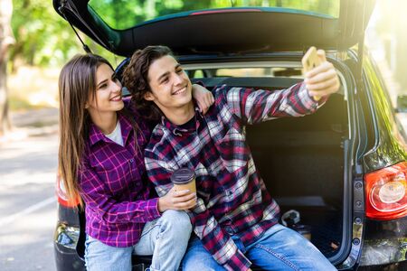 Beautiful young couple taking selfie in car trunk