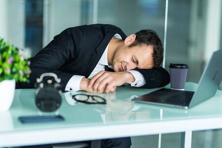 Tired businessman sitting in the office and working on laptop. Businessman sleep and making successful business.の写真素材