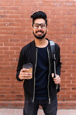 Handsome indian man with backpack and takeaway coffee on street