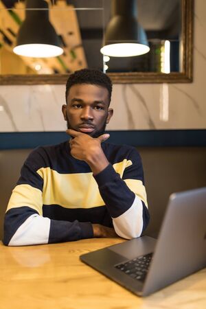 Young african man working over laptop while sitting in cafeの写真素材