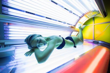 Pretty woman or cute girl with sexy healthy body lying in solarium spa salon in bikini and sunglassesの写真素材