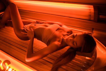 young woman at laying on solarium bed and get brown skin tone ready for summerの写真素材