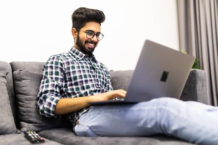 Indian man relaxing on sofa with laptop at homeの写真素材