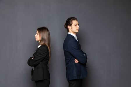 Business man and woman standing back to back isolated on gray background.の写真素材