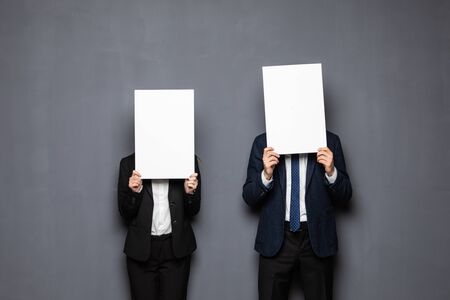 Business couple holding paper over their faces on grayの写真素材