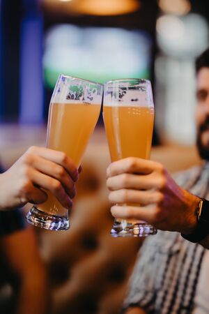 Close up of hands of two friends toasting with glasses of beer at the pub.の写真素材