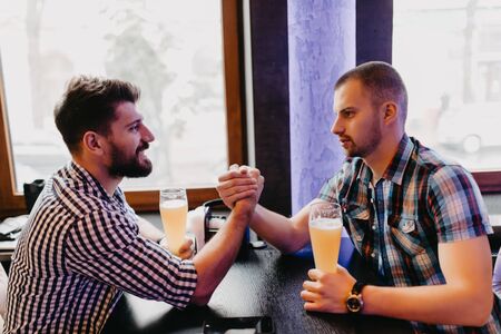 happy male friends drinking beer and have hands fight at pubの写真素材