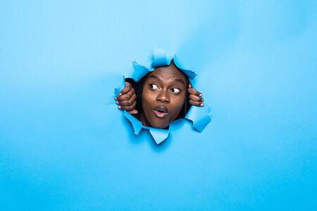 Young african woman posing from blue paper holeの写真素材