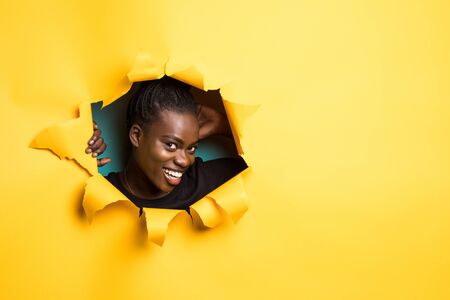 Young afro american woman posing from yellow paper holeの写真素材