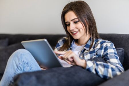 Woman relaxing on a sofa while touching a tablet in a living room