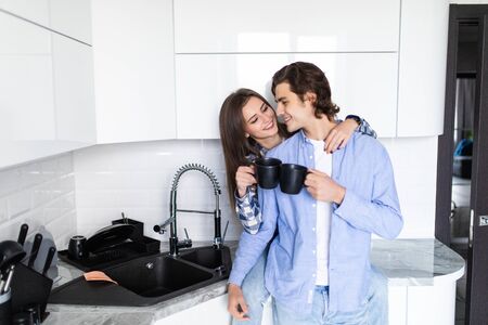 Young man and woman family standing in the kitchen together hugging kissing driking coffee holding cupsの写真素材