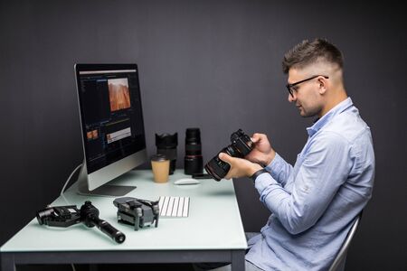 COnfident photographer. Cheerful young man holding digital camera while sitting at his working placeの写真素材