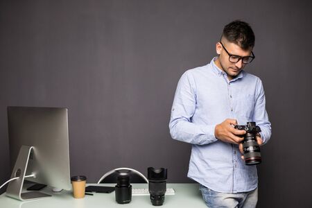 Cheerful young man holding digital camera and smiling while sitting at his working placeの写真素材