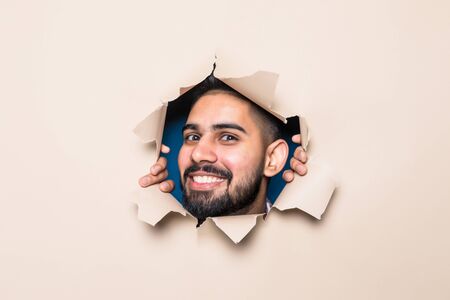 Young indian bearded man smile look from beige paper hole