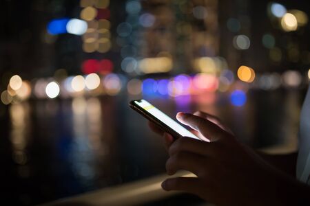 Close-up image of male hands using smartphone at night on city shopping street. Searching or social networks conceptの写真素材