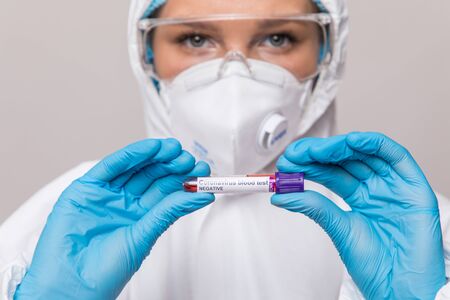 Female doctor in protective suit and face shield holding negative blood test result for coronavirus...