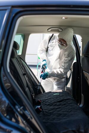 Disinfector in protective suit conducts disinfection in contaminated area of car to prevent coronavirus. Health care.