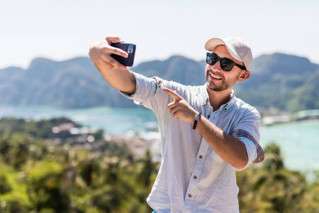 Handsome young man make video call on the phone enjoying the view in phi phi island view point.の写真素材