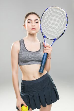 Cropped image of a confident woman tennis player holding racket and ball isolated over gray backgroundの写真素材