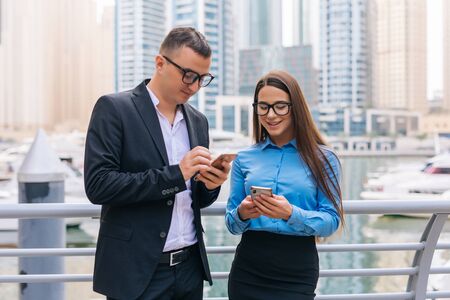 Two smiling business workers with mobile phone in hands are having pleasant conversation on...