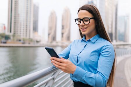 Young business woman texting on a mobile phone outdoors on skyscrapers backgroundの写真素材