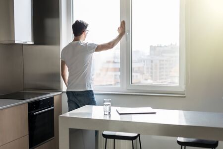Young man looking out the window while holding glass with teaの写真素材