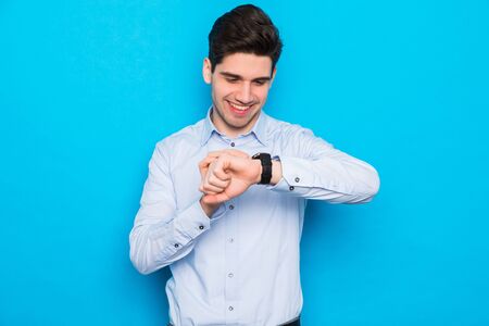 Young handsome man over isolated blue background showing the hand watch