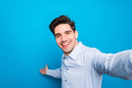 Handsome brunet young man is making selfie and smiling on blue backgroundの写真素材