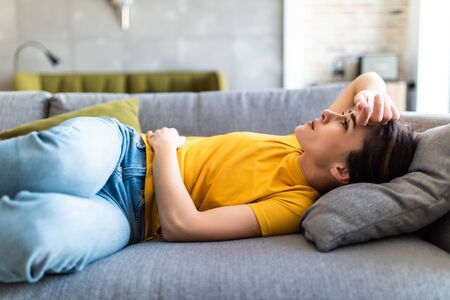 Sick woman lying on sofa in the living room with stomahc acheの写真素材