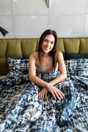 Smiling brunette woman sitting on her bed in her bedroom