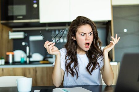 Image of shocked cute young pretty woman standing in kitchen indoors at home using laptop computer cooking.の写真素材