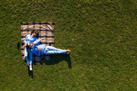 Young couple lying on the grass and looking up in the park. Top view on the lying couple from the tree.の写真素材
