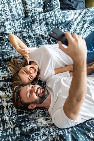 Top view of beautiful young loving couple lying in bed and making selfie