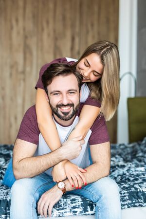 Beautiful young couple having fun in bedroom at home while shirtless man giving his girlfriend piggy back rideの写真素材