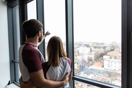 Rear view young couple embracing and pointing at something and look away windowの写真素材
