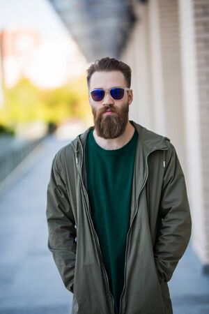 Young man with a beard and mustache with glasses posing on the street, outdoor portrait.
