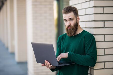 Cheerful bearded male entrepreneur with modern laptop outside building on city street