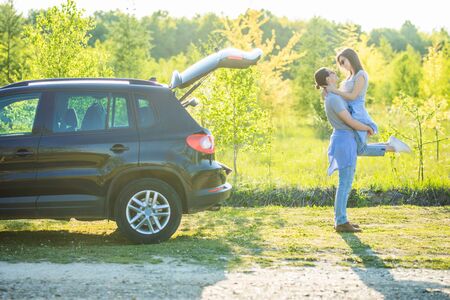 Young man carrying a woman on his back near car while on a road trip.の写真素材